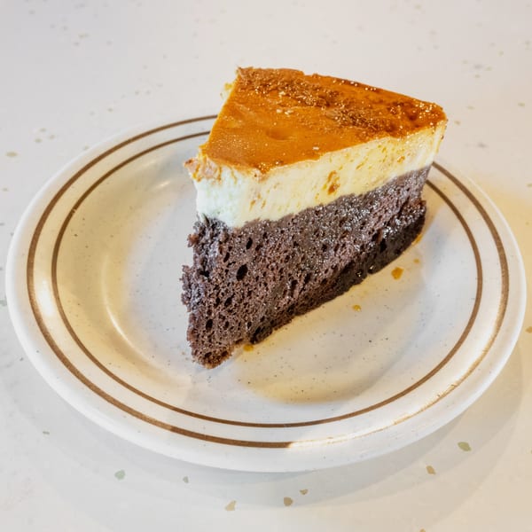 A slice of chocolate flan cake with a golden caramel topping on a white plate.