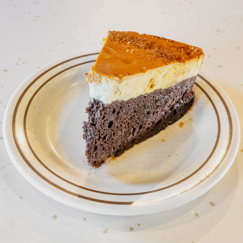 A slice of chocolate flan cake with a golden caramel topping on a white plate.