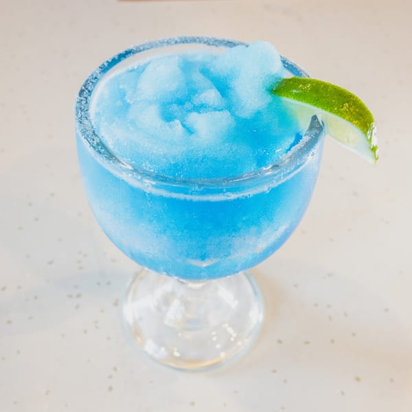 Bright blue frozen margarita in a sugar-rimmed glass, garnished with a fresh lime wedge.