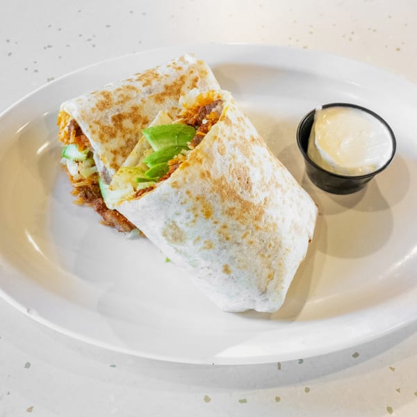 Two burritos with meat, avocado, and lettuce, served with a side of white sauce.