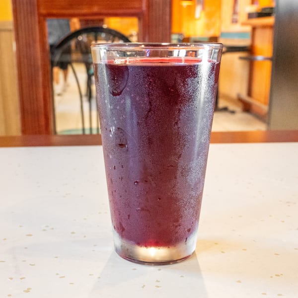 A cold glass of purple juice with condensation sits on a speckled white table.