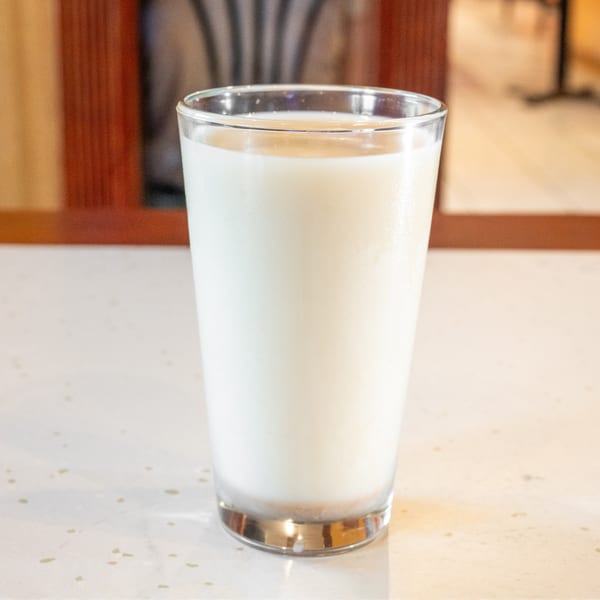 A clear glass filled with white milk sits on a light-colored speckled countertop.