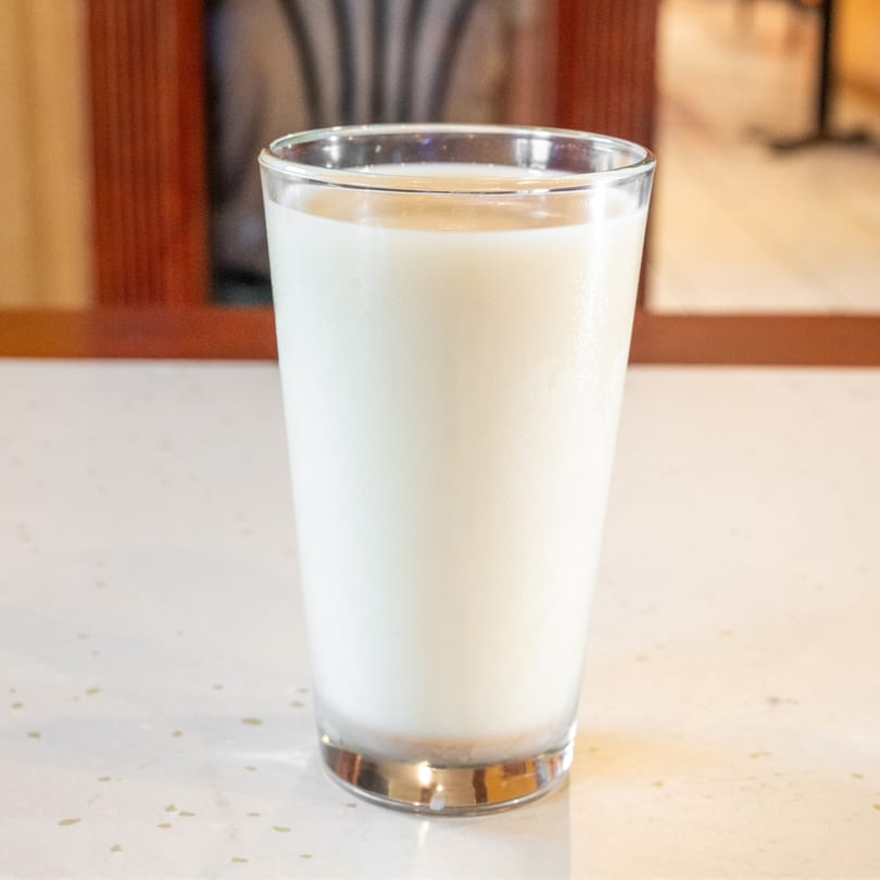 A clear glass filled with white milk sits on a light-colored speckled countertop.